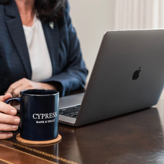 Persona usando una laptop con una taza de Cypress Bank