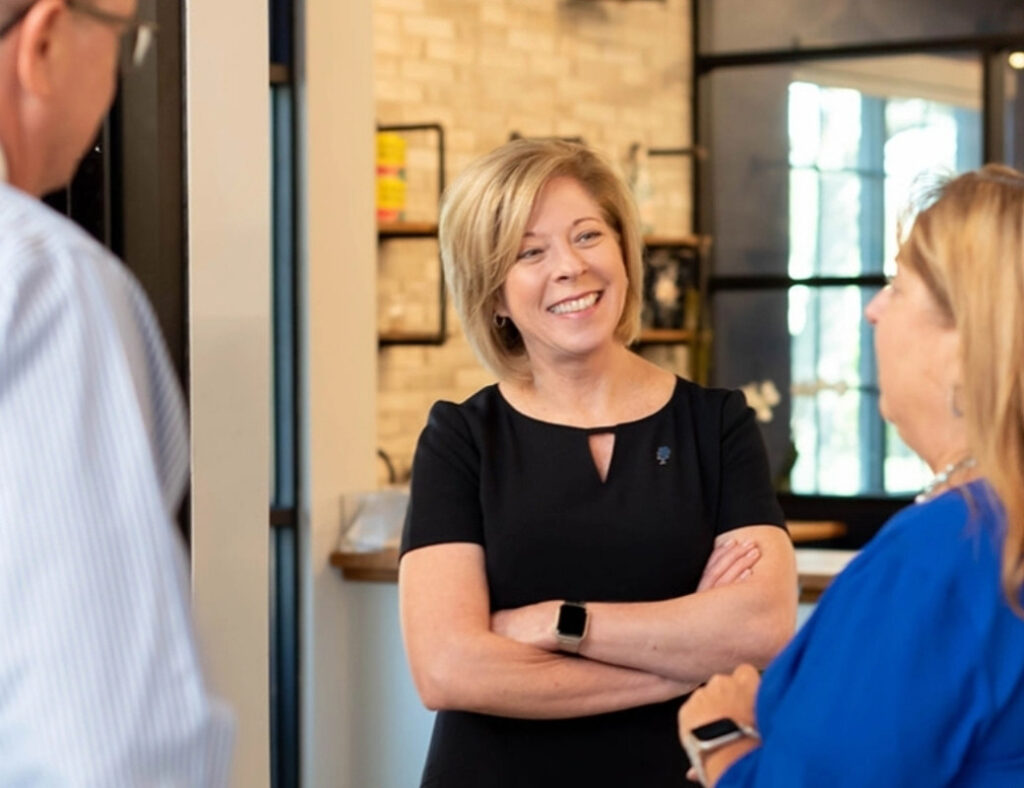 Mujer sonriendo hablando con dos personas en un evento.