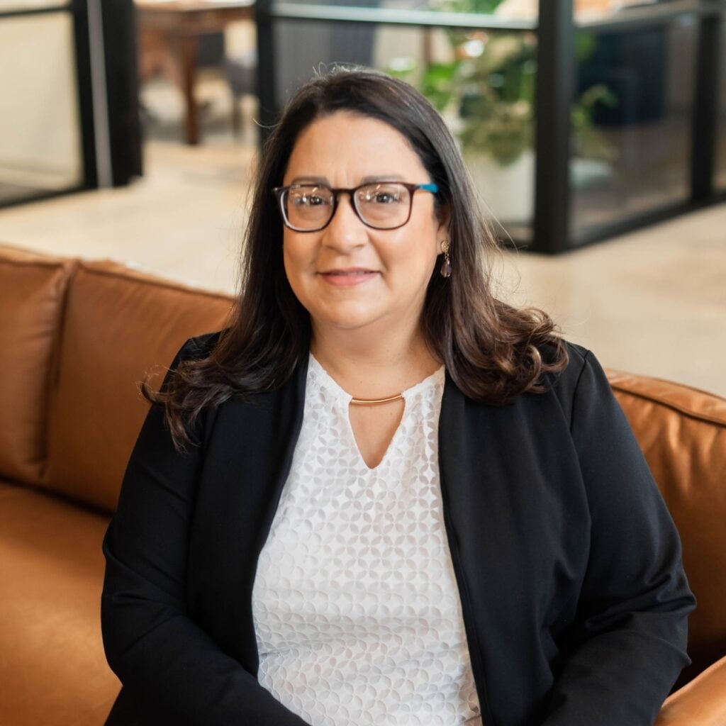 Person sitting on brown couch, smiling in office setting.