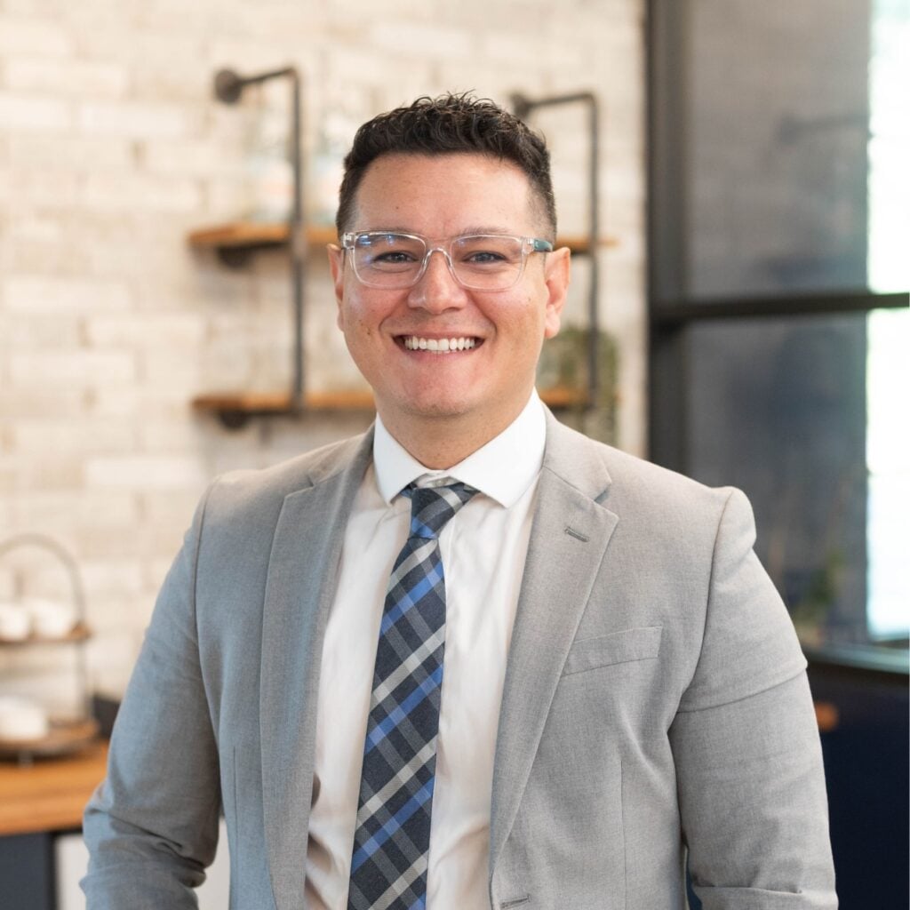 Smiling person in glasses and suit indoors.