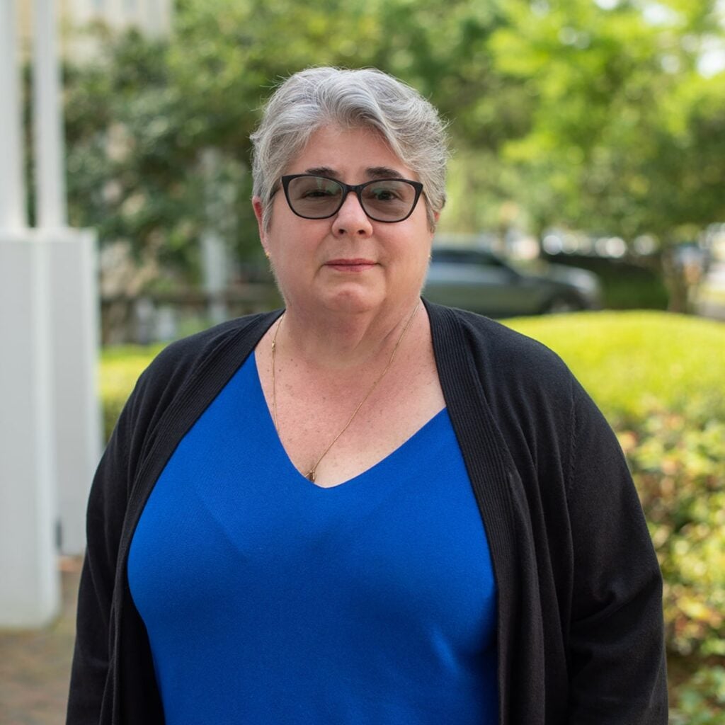 Woman in blue top outside with green background.