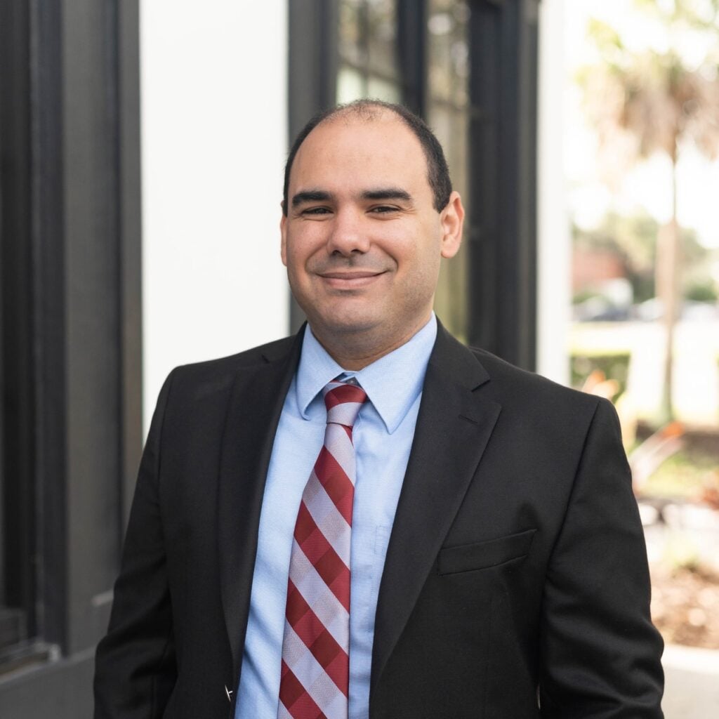 Smiling man in suit and tie outside building.