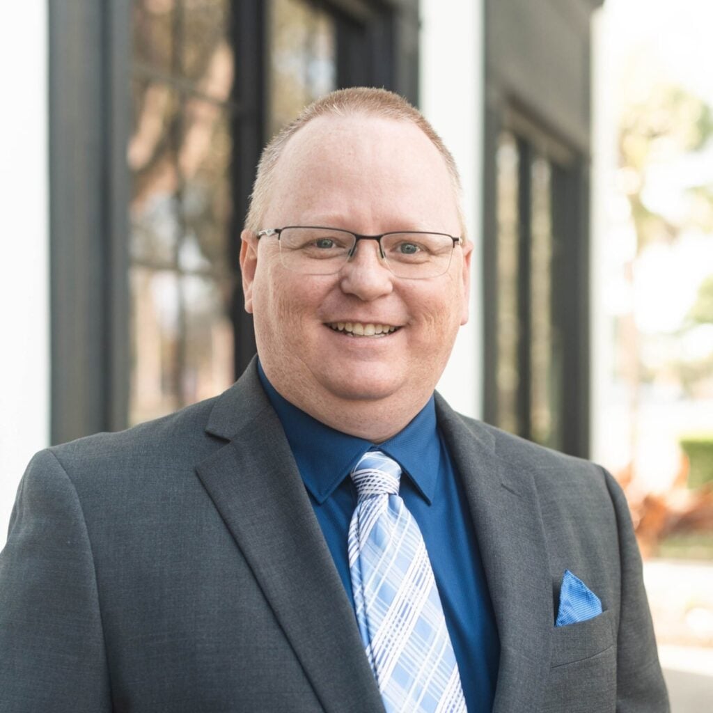 Smiling person in suit and tie outdoors.