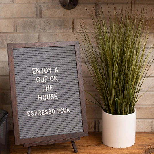 Señal de hora de espresso junto a la planta en la mesa.