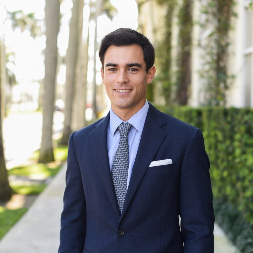 Smiling man in suit outdoors with trees background.