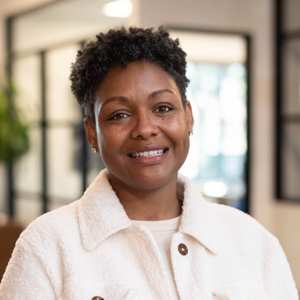 Smiling person in a white jacket indoors.