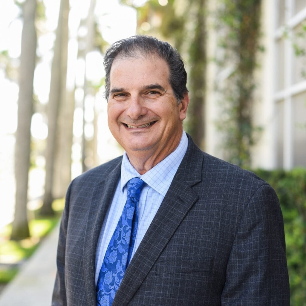 Smiling man in suit with blue tie outside.