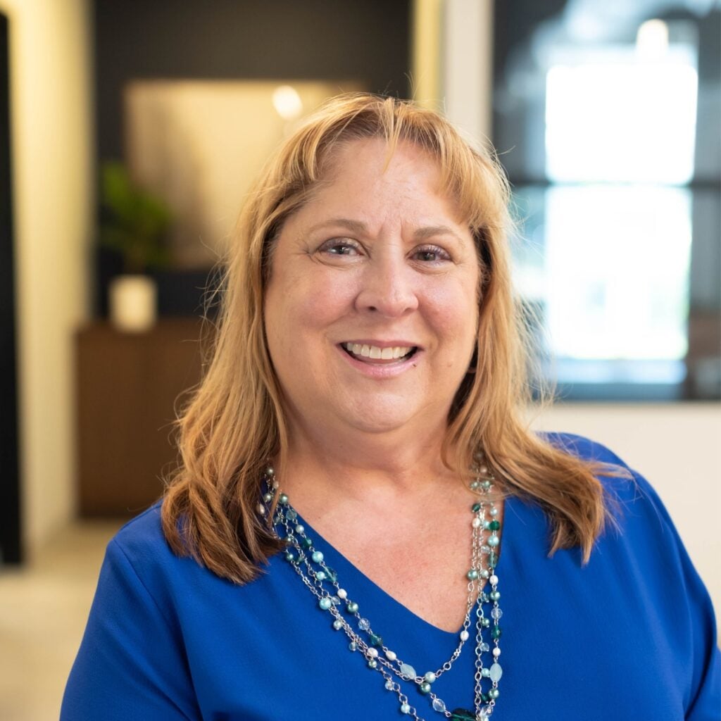 Smiling woman in office, wearing blue shirt.