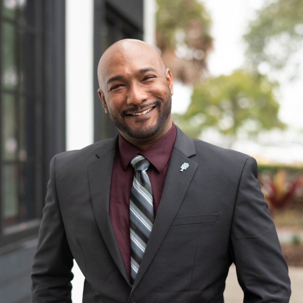 Smiling man in suit and tie outside building.