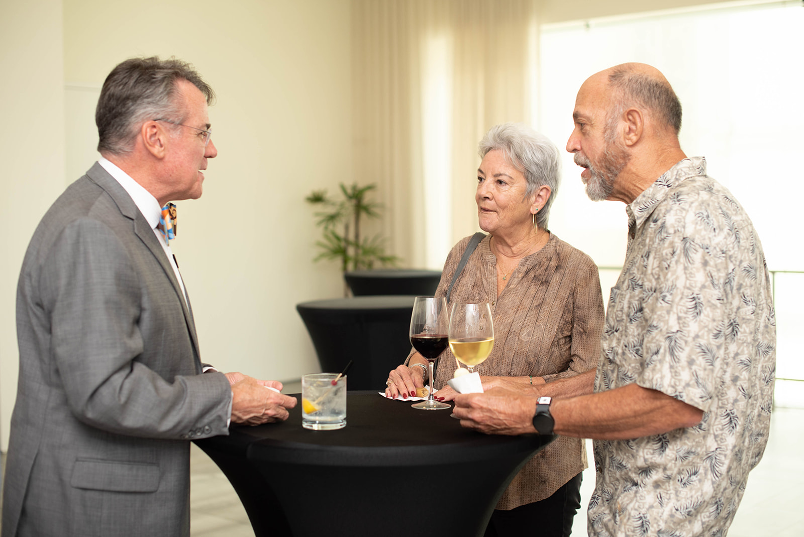 Tres adultos conversan alrededor de una mesa de cóctel con bebidas.