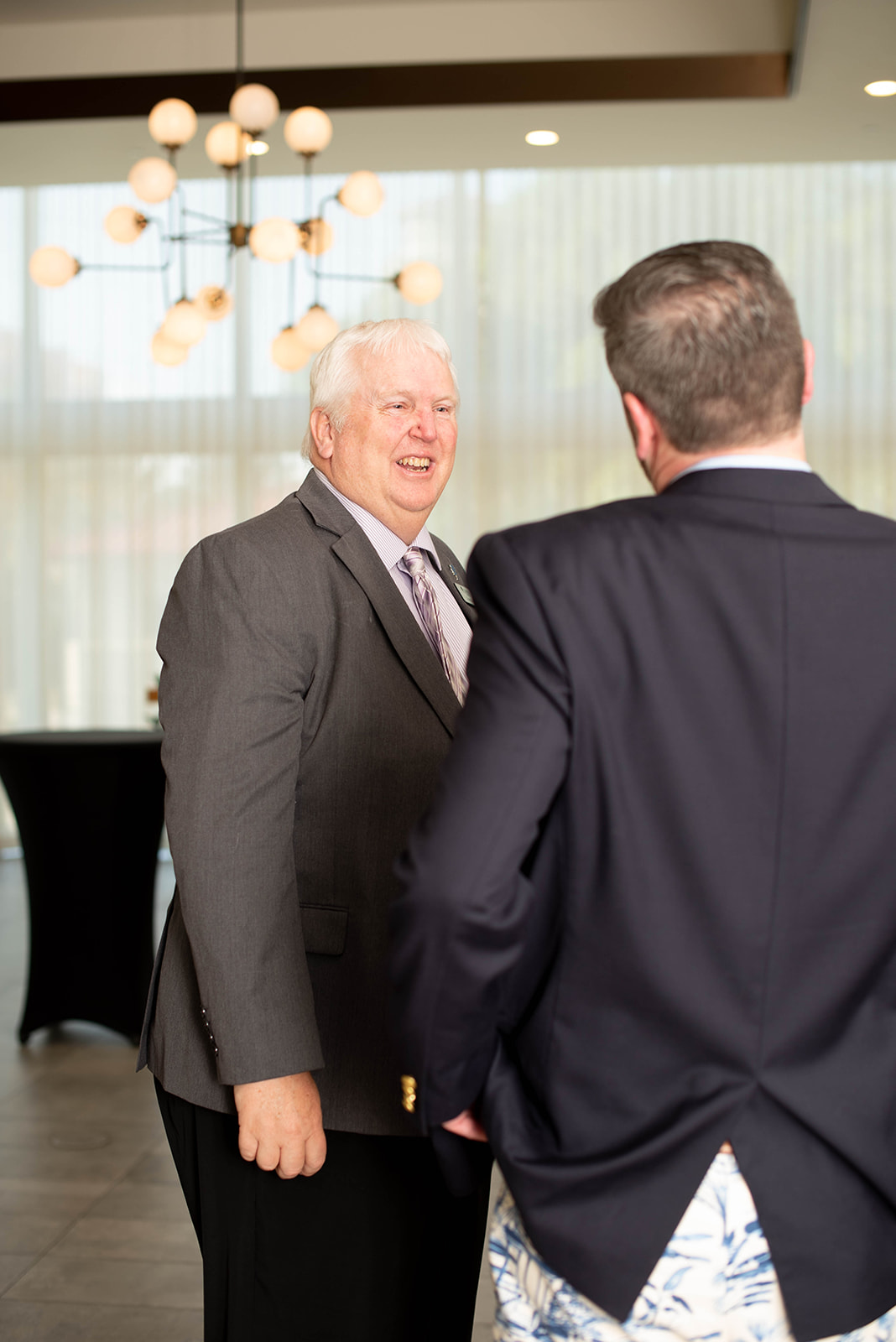 Dos hombres con traje conversan en un lugar de eventos moderno.