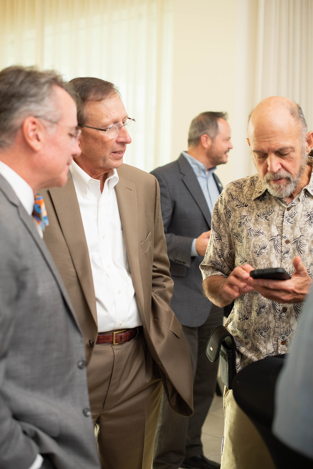 Cuatro hombres conversan en interiores, uno usando un teléfono inteligente.