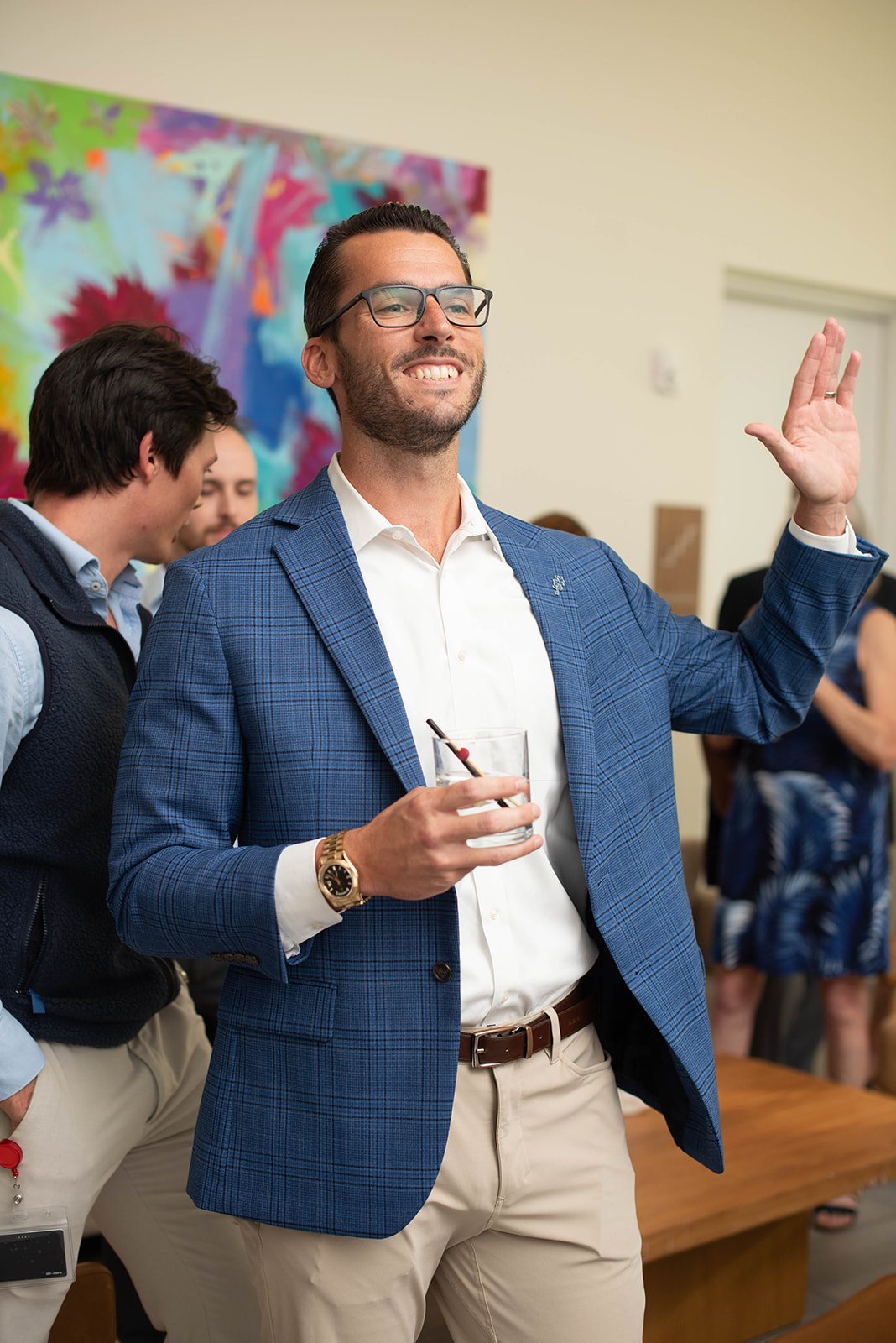 Hombre sonriendo con blazer azul levanta la mano en una fiesta