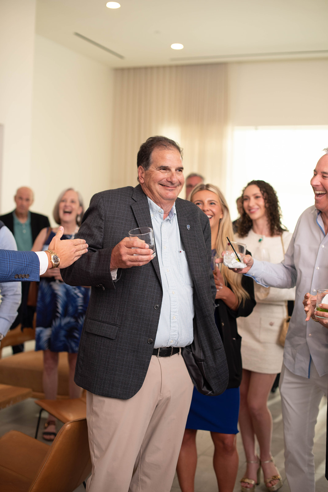 Hombre sonriendo sostiene una bebida en una animada reunión en interiores