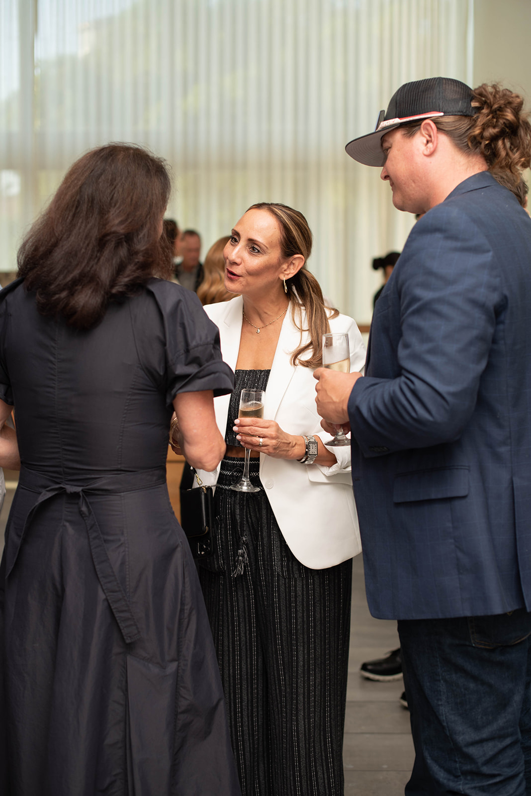 Tres invitados conversan mientras sostienen champán en un evento en interiores.