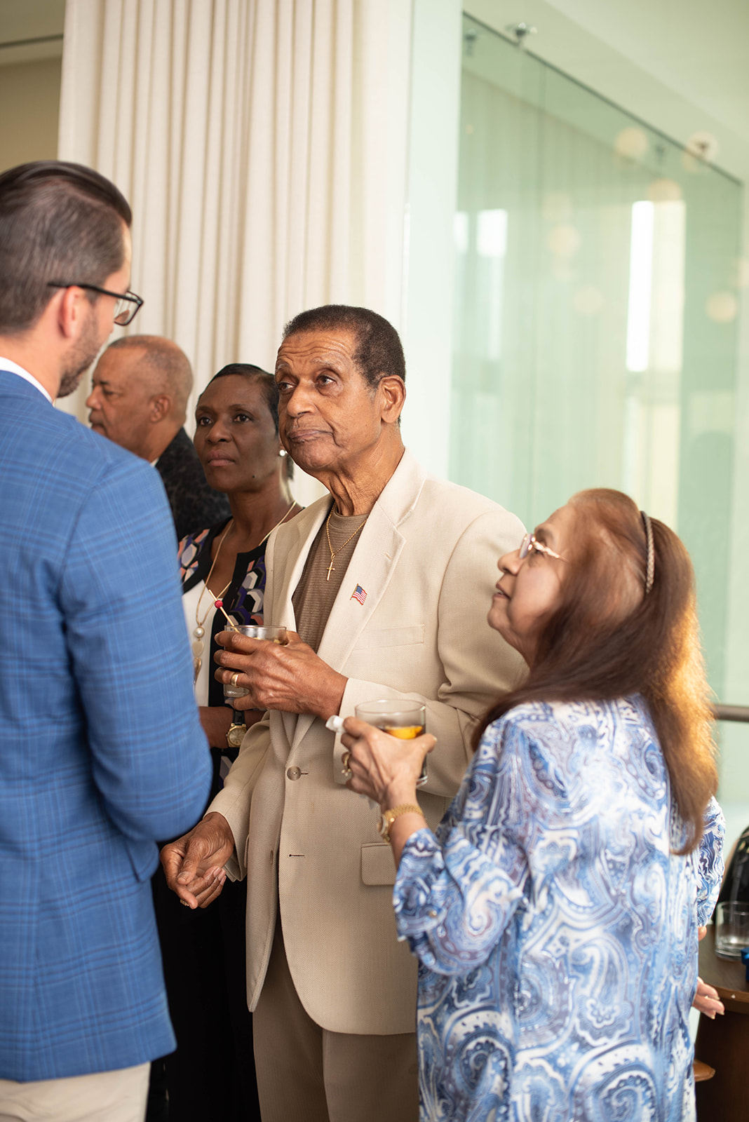 Los invitados conversan en una recepción interior mientras sostienen bebidas.