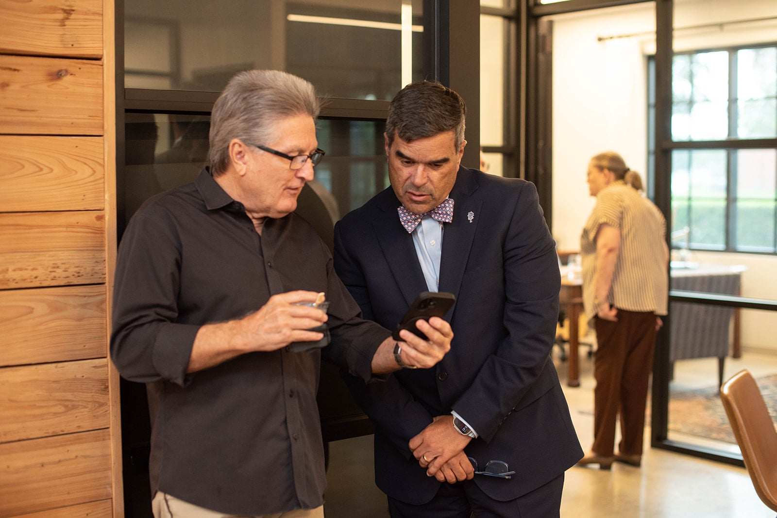 Dos hombres examinan un teléfono inteligente en una oficina moderna.