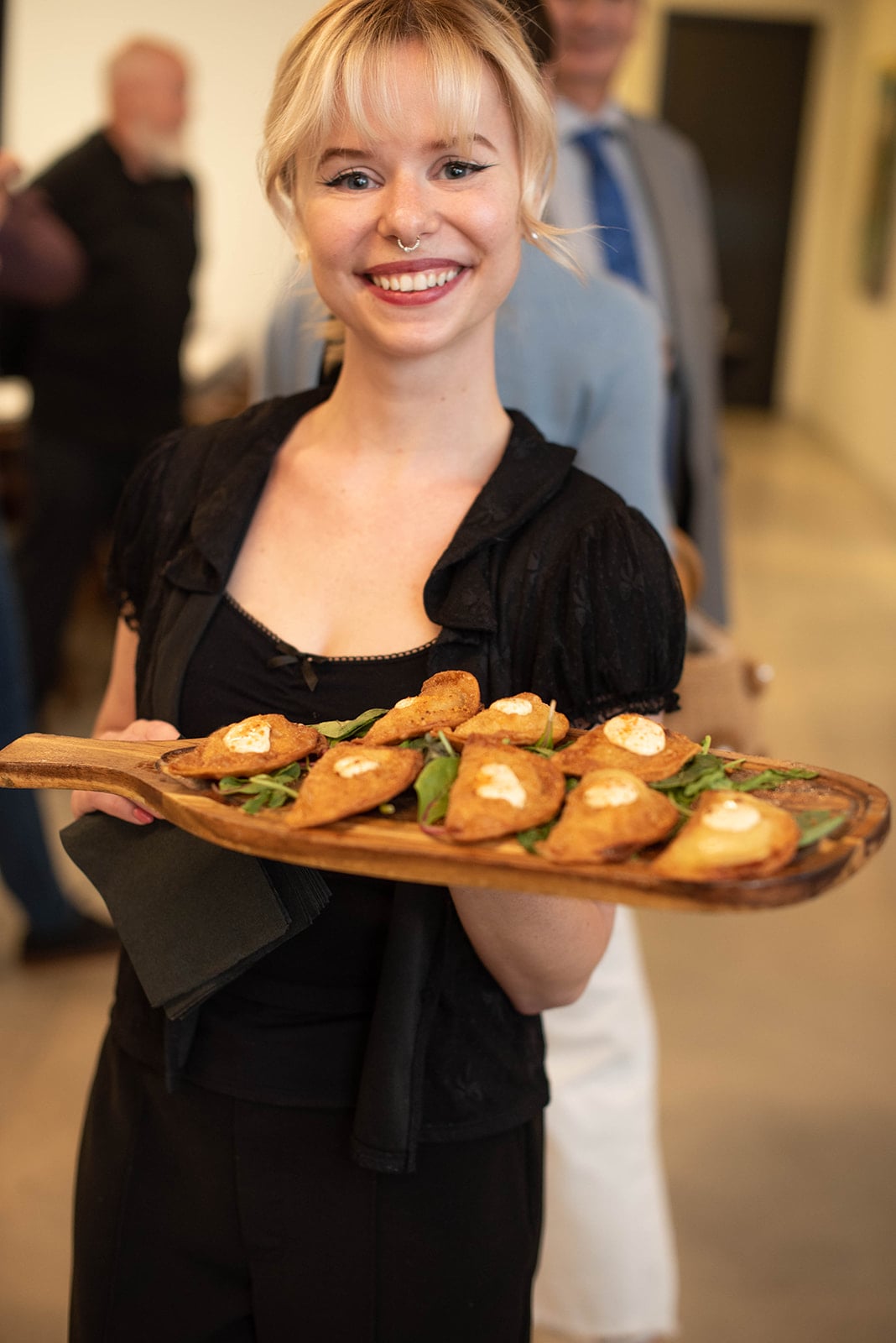 Camarero sonriendo sostiene una bandeja de aperitivos en un evento en interiores