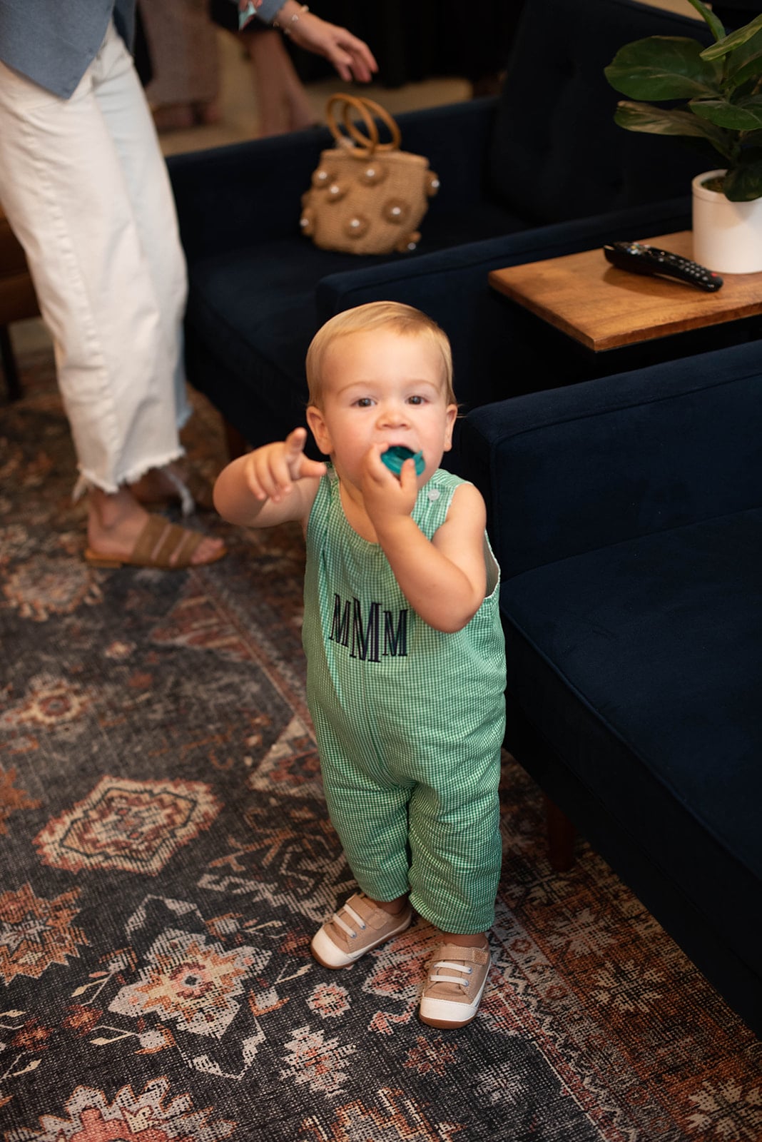 Niño pequeño en mameluco verde de pie junto a un sofá azul marino
