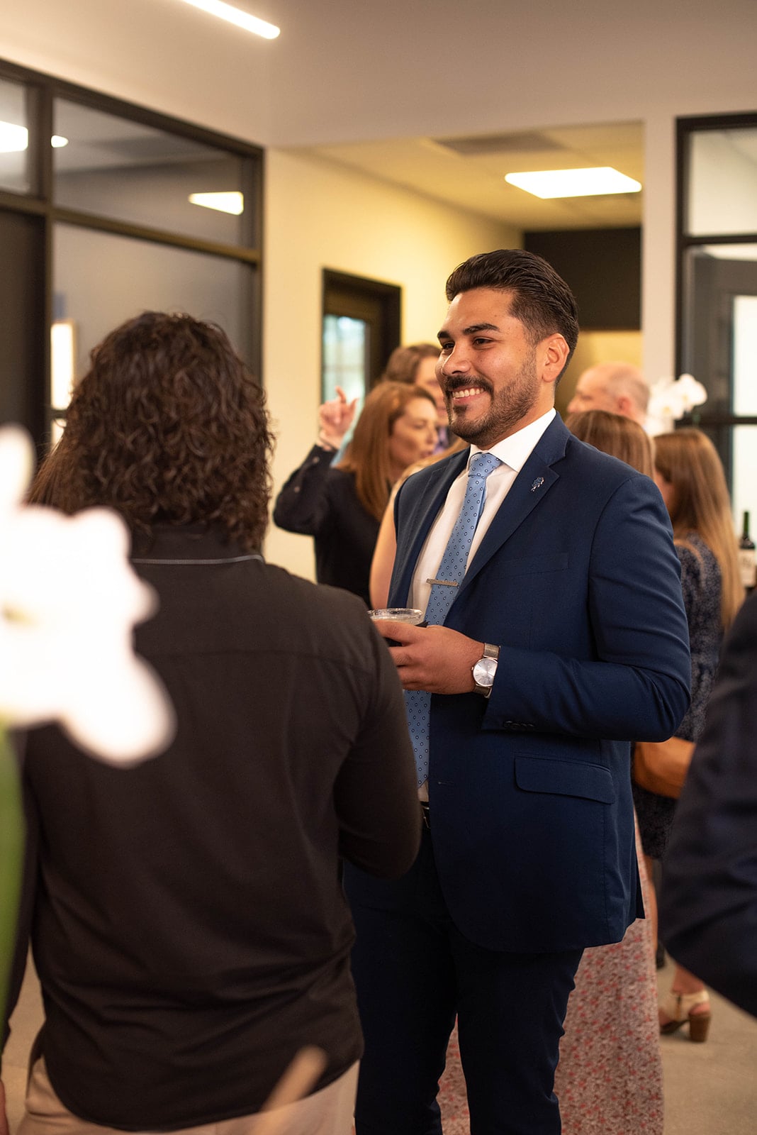Hombre sonriendo en traje azul haciendo contactos en un evento en interiores